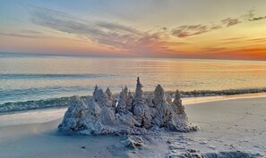 Ein Sandstrand mit einer großen Sandburg im Vordergrund.