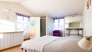 Une chambre à coucher avec un lit, une chaise, une coiffeuse avec un miroir et une fenêtre avec des rideaux.
