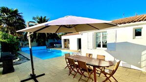 Une terrasse avec une piscine, une table et des chaises d’extérieur, et un parasol.