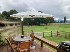 A wooden deck with a round table and chairs, a white umbrella, and a barbecue grill. - Country tiny house with spa (Arapuni)