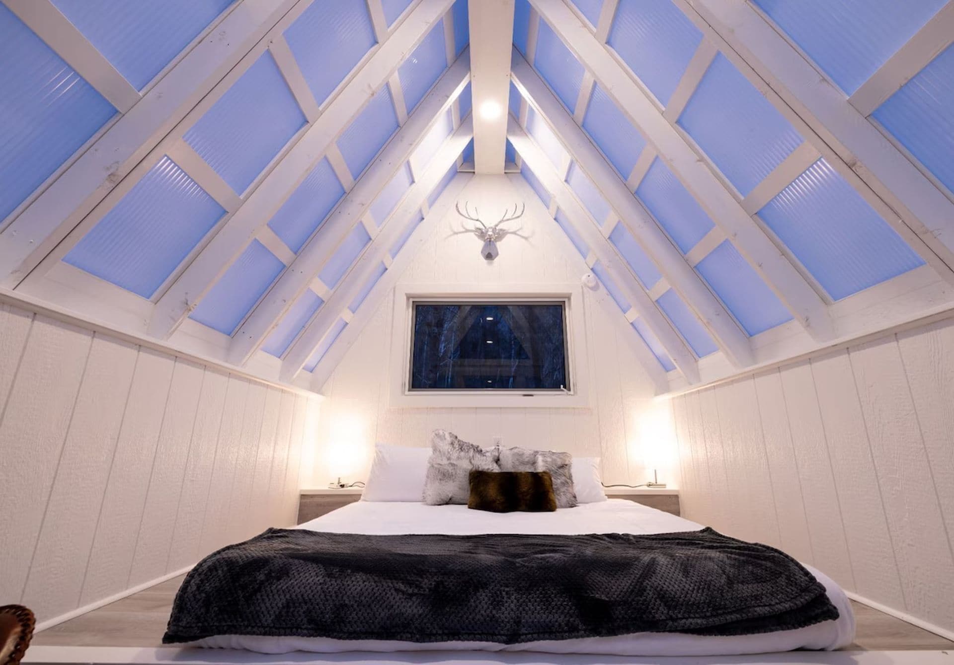 A bedroom with a skylight, a bed, a nightstand, and a wall-mounted light fixture.
