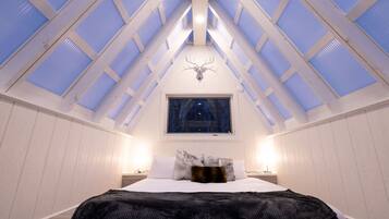 A bedroom with a skylight, a bed, a nightstand, and a wall-mounted light fixture.
