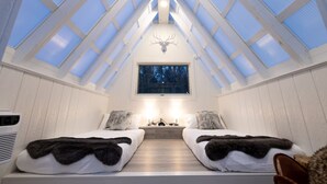 A room with a sloped ceiling, two beds with fur throws, a mounted deer head, and a window with a forest view. - The Glo Haus @ Four Fillies Lodge (Peterstown)