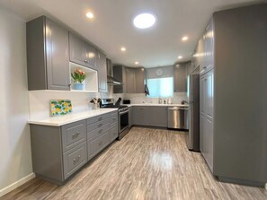 A modern kitchen with grey cabinets, stainless steel appliances, and a wooden floor.