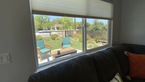 A living room with a large window, a dark sofa, and a view of a backyard with outdoor furniture.