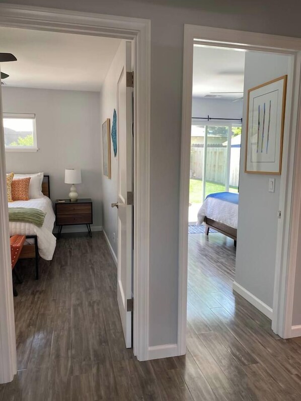 A hallway leading to a bedroom with a bed, a nightstand, and a lamp.