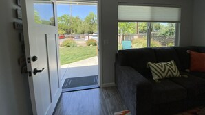 A room with a dark-colored sofa, a sliding glass door leading to a patio, and a window with a blind.