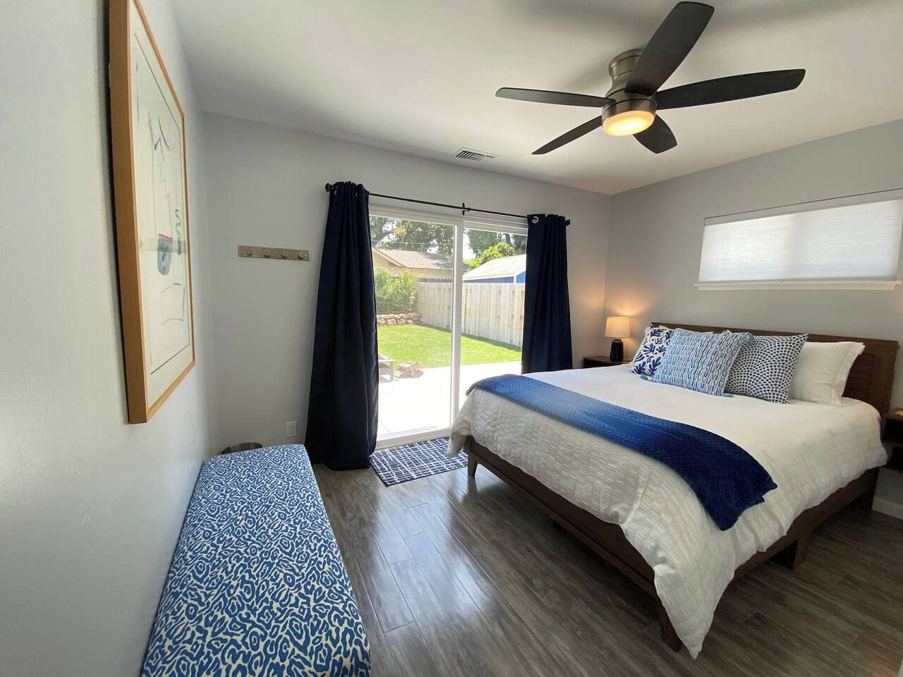 Un dormitorio con cama, ventilador de techo, ventana con cortinas y vistas al exterior.