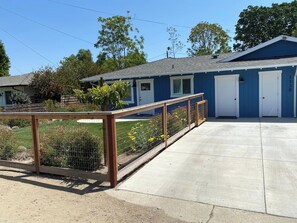 Un motel con un patio trasero cercado, un camino de acceso de concreto y un edificio azul con puertas blancas.