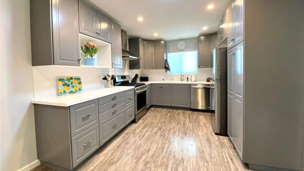 A modern kitchen with grey cabinets, a stainless steel dishwasher, and a built-in oven.