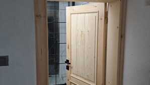 Eine Holztür mit einfachem Riegel, die zu einem Raum mit weißen Wänden und Fliesenboden führt.