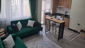 Ein modernes Wohnzimmer mit einem grünen Sofa, einem kleinen Holztisch und einer Küchenzeile mit Holdekor und einem Herd.