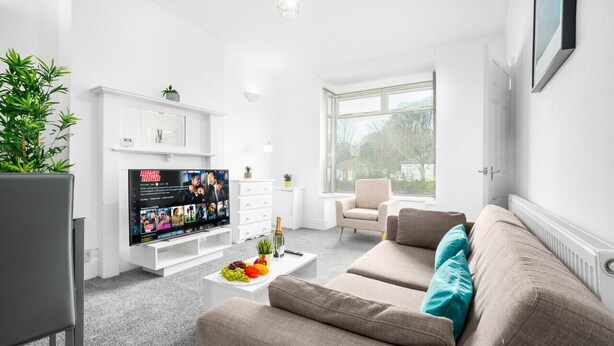 Ein modernes Wohnzimmer mit Flachbildfernseher, einem beigefarbenen Sofa, einem Couchtisch mit Obst und einer Topfpflanze.