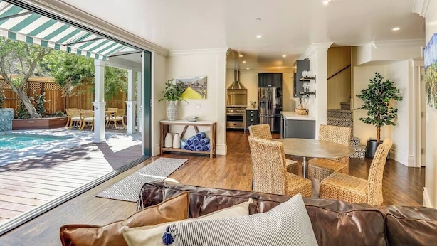 A spacious living area with a large glass door leading to an outdoor patio, a dining area with wicker furniture, and a kitchen with modern appliances.