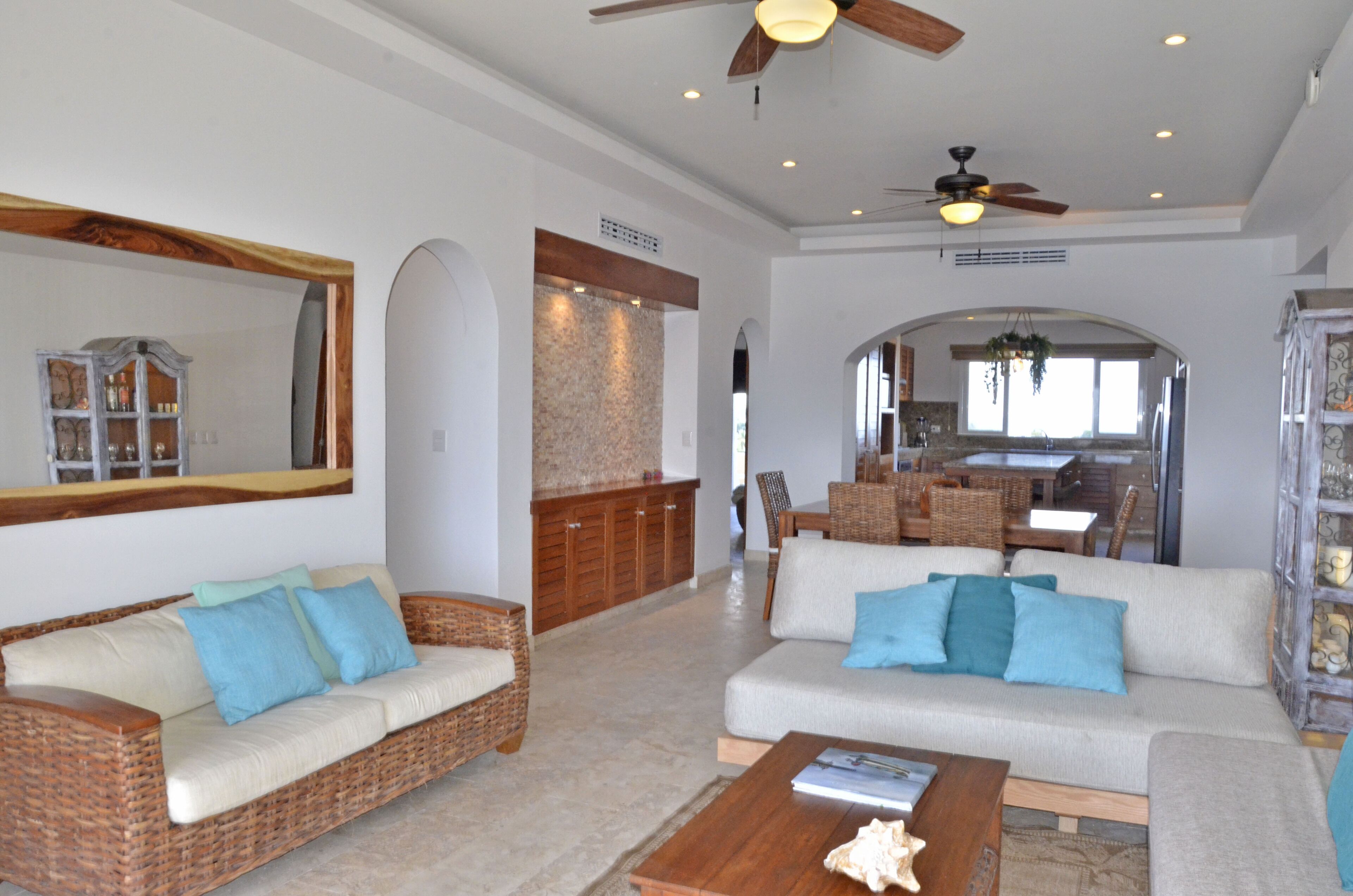 A spacious living room with a large mirror, wicker furniture, and a ceiling fan.