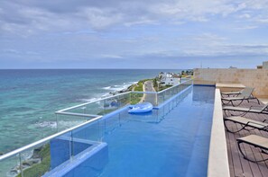 A rooftop infinity pool with a clear view of the ocean, lounge chairs, and a glass balustrade. - Zuperb 3 Bedroom Ocean View Apart Isla Mujeres (Isla Mujeres)