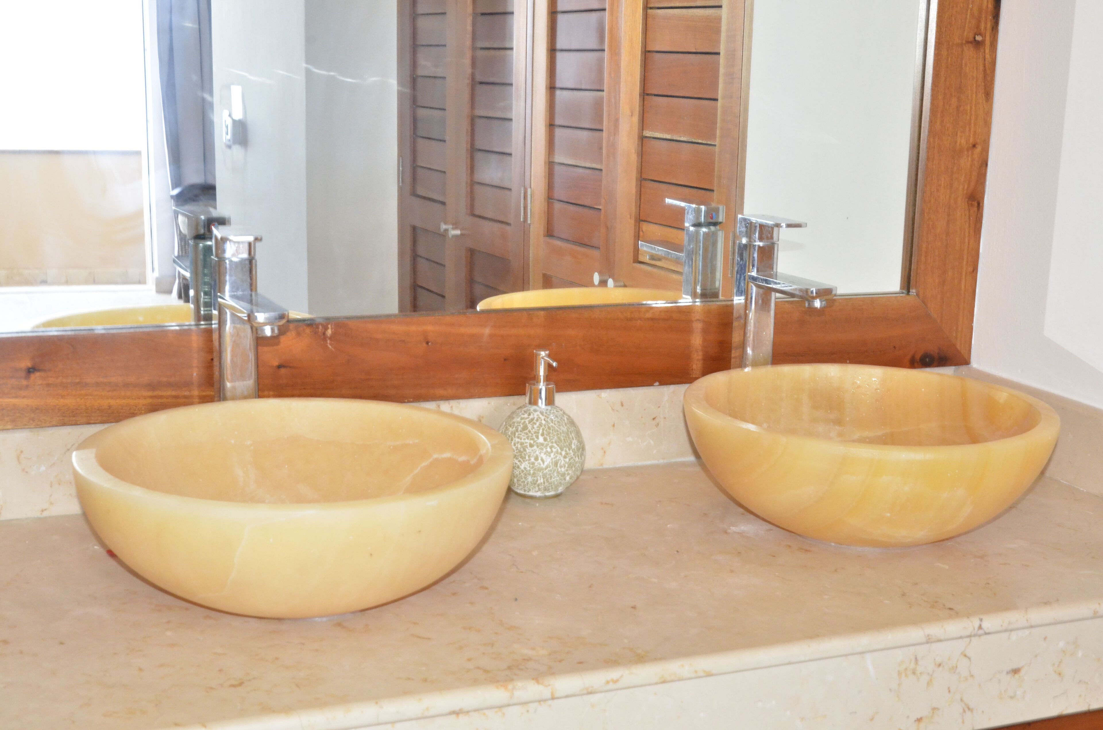 A bathroom with two large beige sinks, a mirror, and wooden doors.