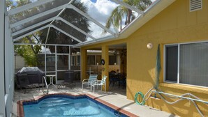 A covered outdoor swimming pool area with lounge chairs and a dining table. - Waterfront adjacent to the Gulf of Mexico (Hudson)