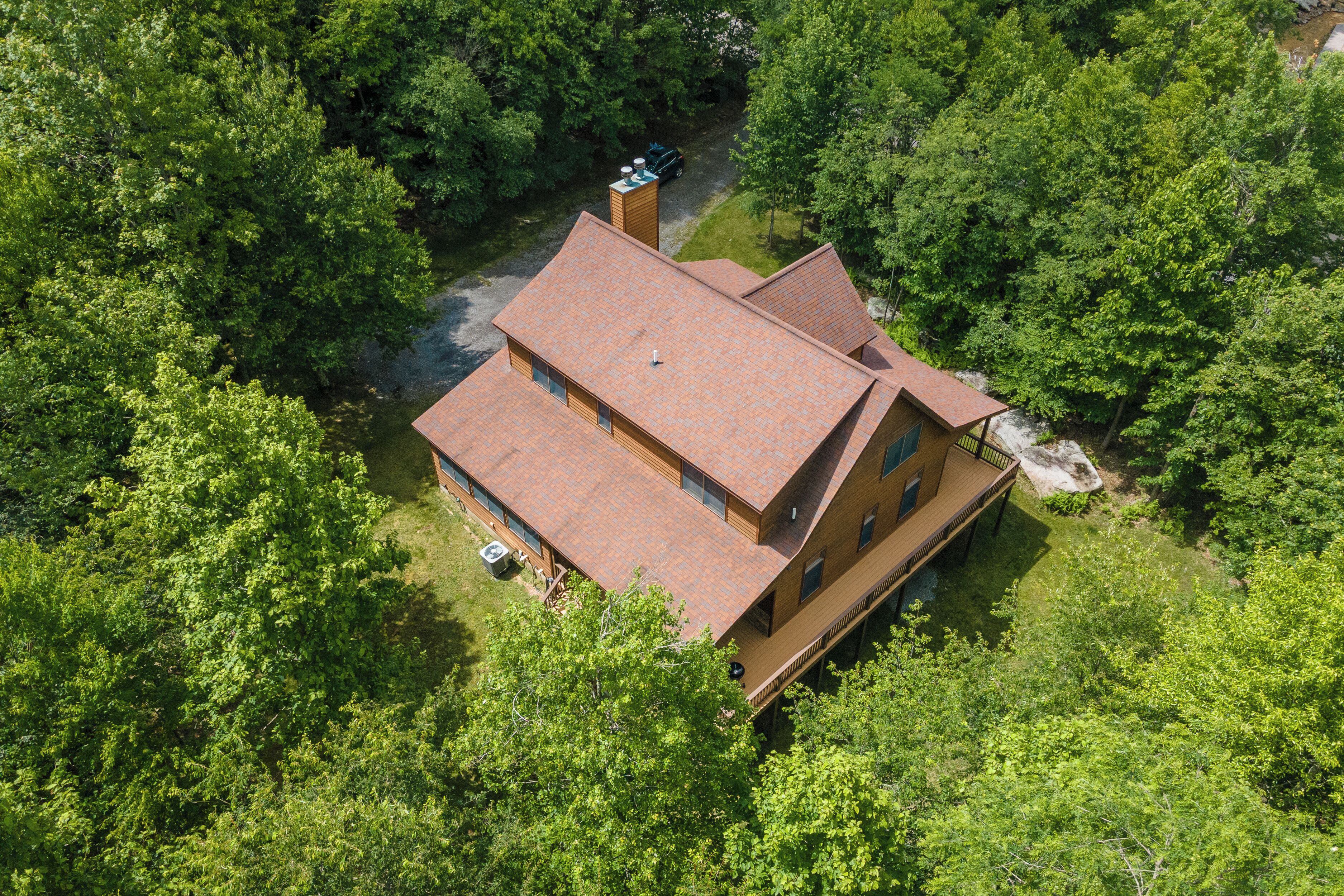 Une maison à deux étages, avec un toit rouge, entourée d’arbres verdoyants et touffus.