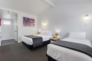 A hotel room with two beds, a desk, a chair, a refrigerator, and a painting on the wall.