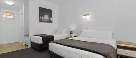 A hotel room with two beds, a bedside table with a lamp, a wall-mounted picture, and a door leading to a bathroom.