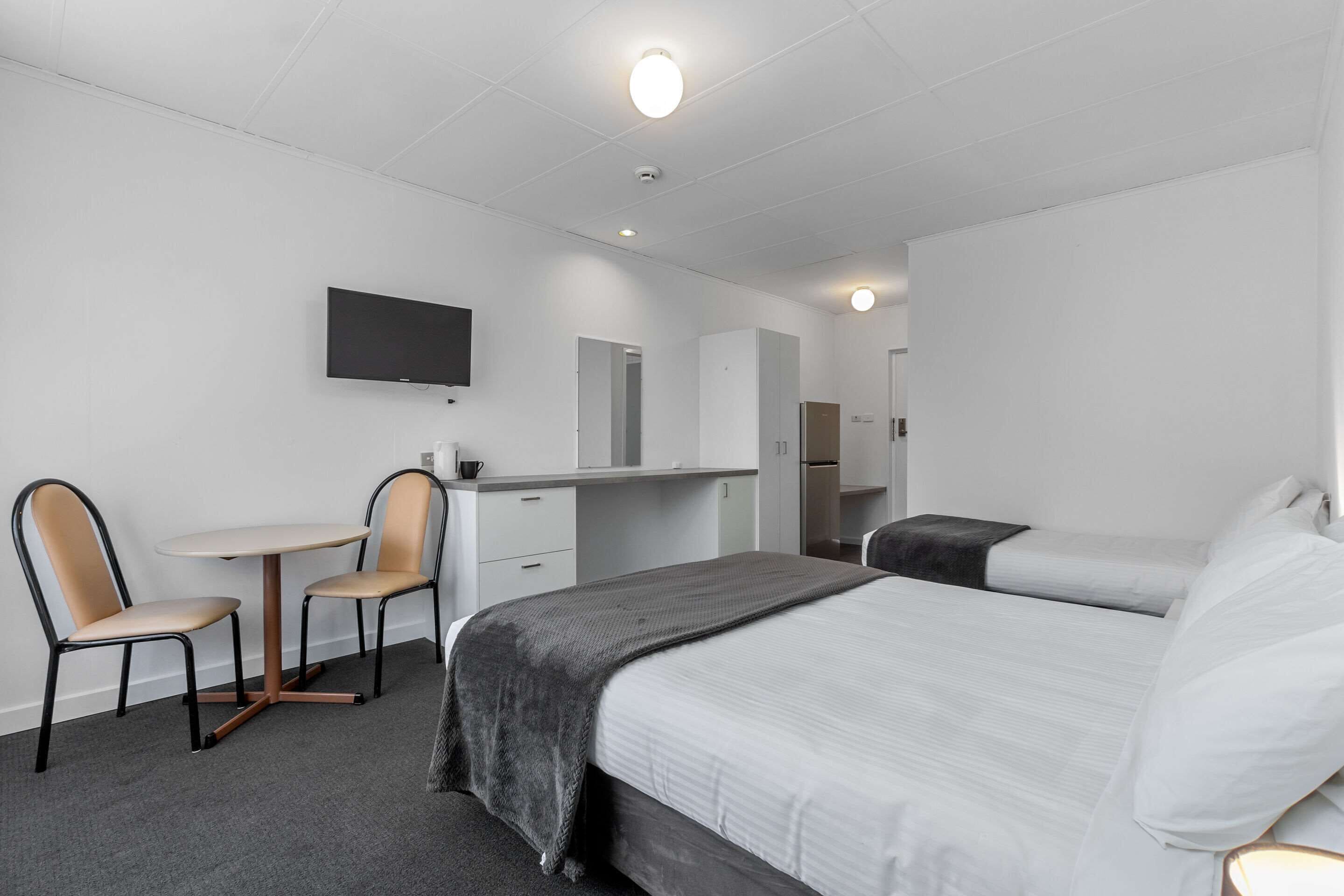 Ein Hotelzimmer mit einem Bett, einem Schreibtisch mit Stuhl, einem Fernseher und einem Kleiderschrank.