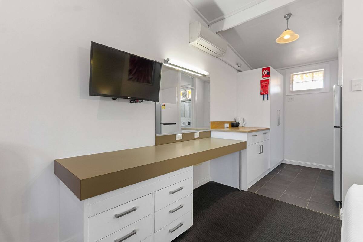 A modern kitchen with a flat-screen TV, white cabinets, a wooden countertop, and a built-in oven.