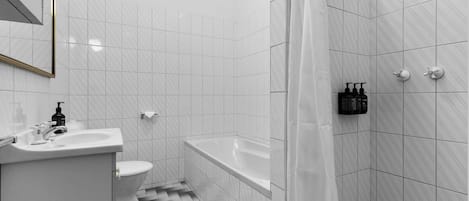 A bathroom with a white sink, toilet, and bathtub, tiled with white and gray tiles.