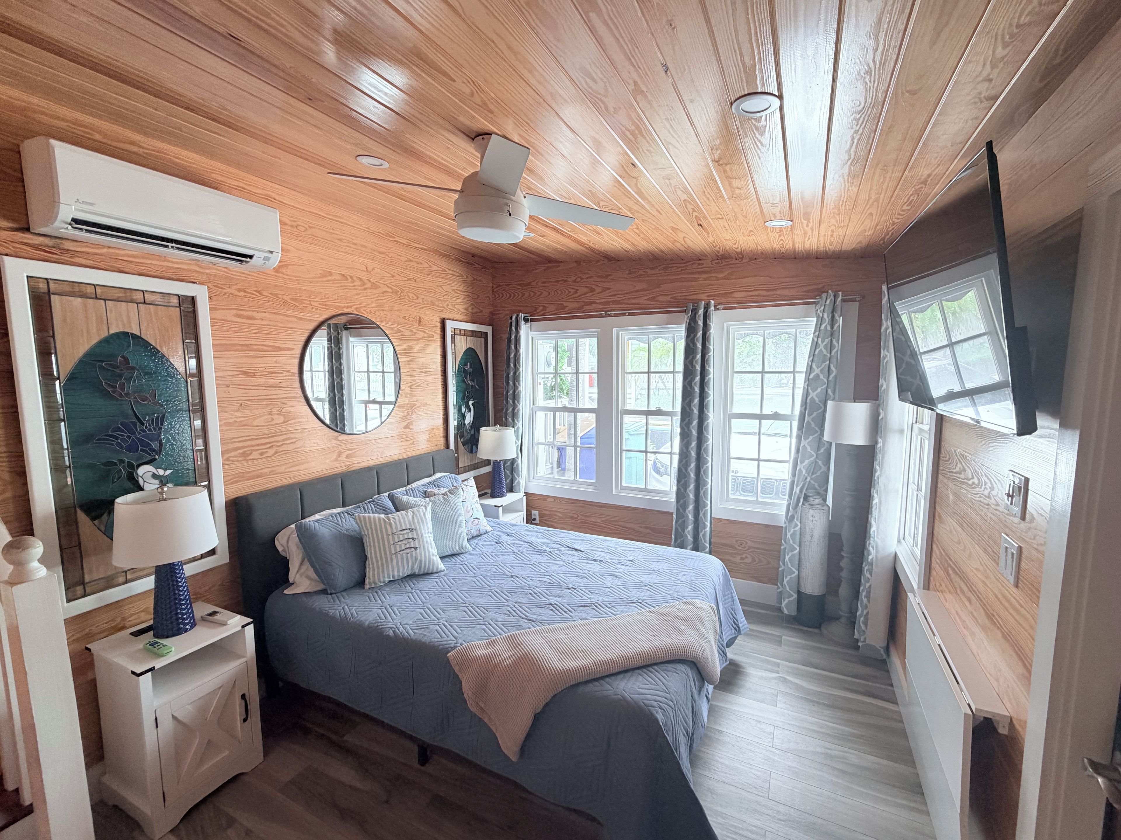 A bedroom with a bed, bedside tables, a ceiling fan, and windows.