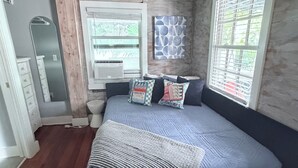 A bedroom with a bed, a window, a wall-mounted air conditioning unit, and a ceiling fan.