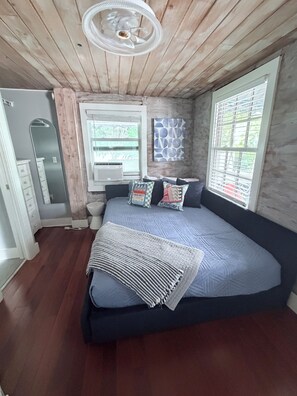 Une chambre à coucher comprenant un lit, une fenêtre, un climatiseur fixé au mur et un ventilateur de plafond.