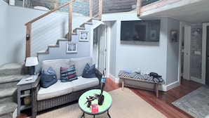 A spacious living area with a high ceiling, a staircase, a sofa with cushions, a small table, and a television mounted on the wall.