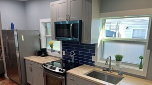 A modern kitchen with grey cabinets, a black microwave, a stainless steel refrigerator, a gas stove, and a sink.