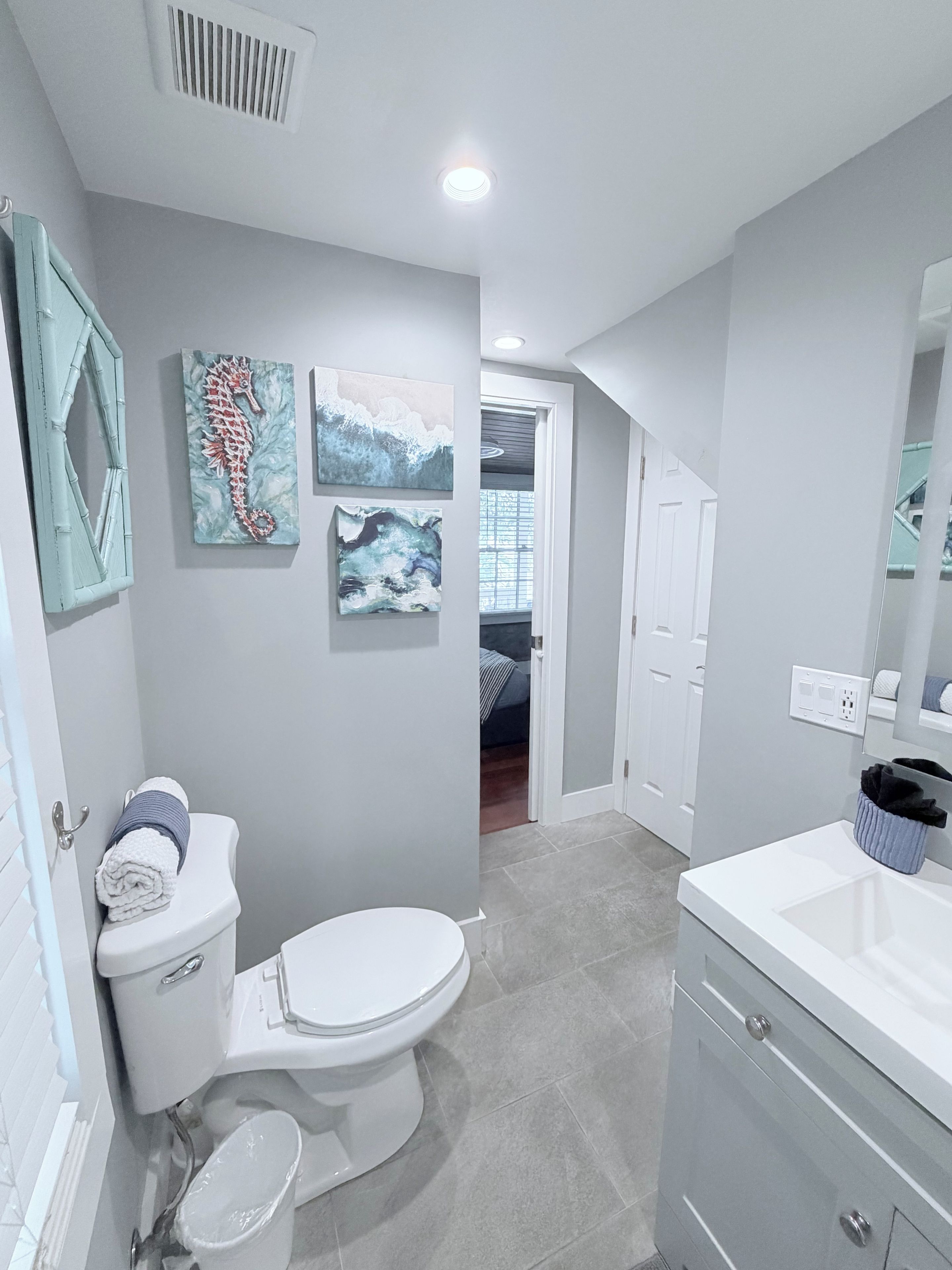 A modern bathroom with a toilet, sink, and a shower area. There are wall-mounted artworks and a mirror above the sink.