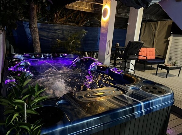 Un jacuzzi con calentador integrado y luces LED, rodeado de mobiliario de exterior y plantas.