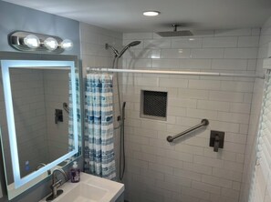 A bathroom with a white tiled shower, a glass shower enclosure, a mirror with lights, and a handrail. - Old Town Key West Cottage 3bed/2bath (Key West)