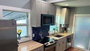 A modern kitchen with grey cabinets, a black microwave, a stainless steel refrigerator, a black stove, and a tiled backsplash. - Old Town Key West Cottage 3bed/2bath (Key West)