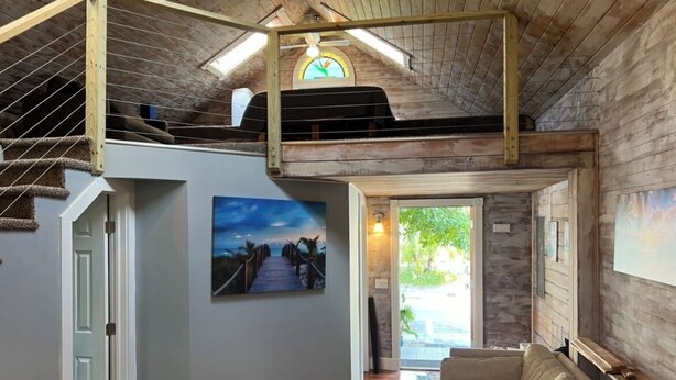 A loft-style living area with a staircase, a large painting, and a view through a glass door. - Old Town Key West Cottage 3bed/2bath (Key West)