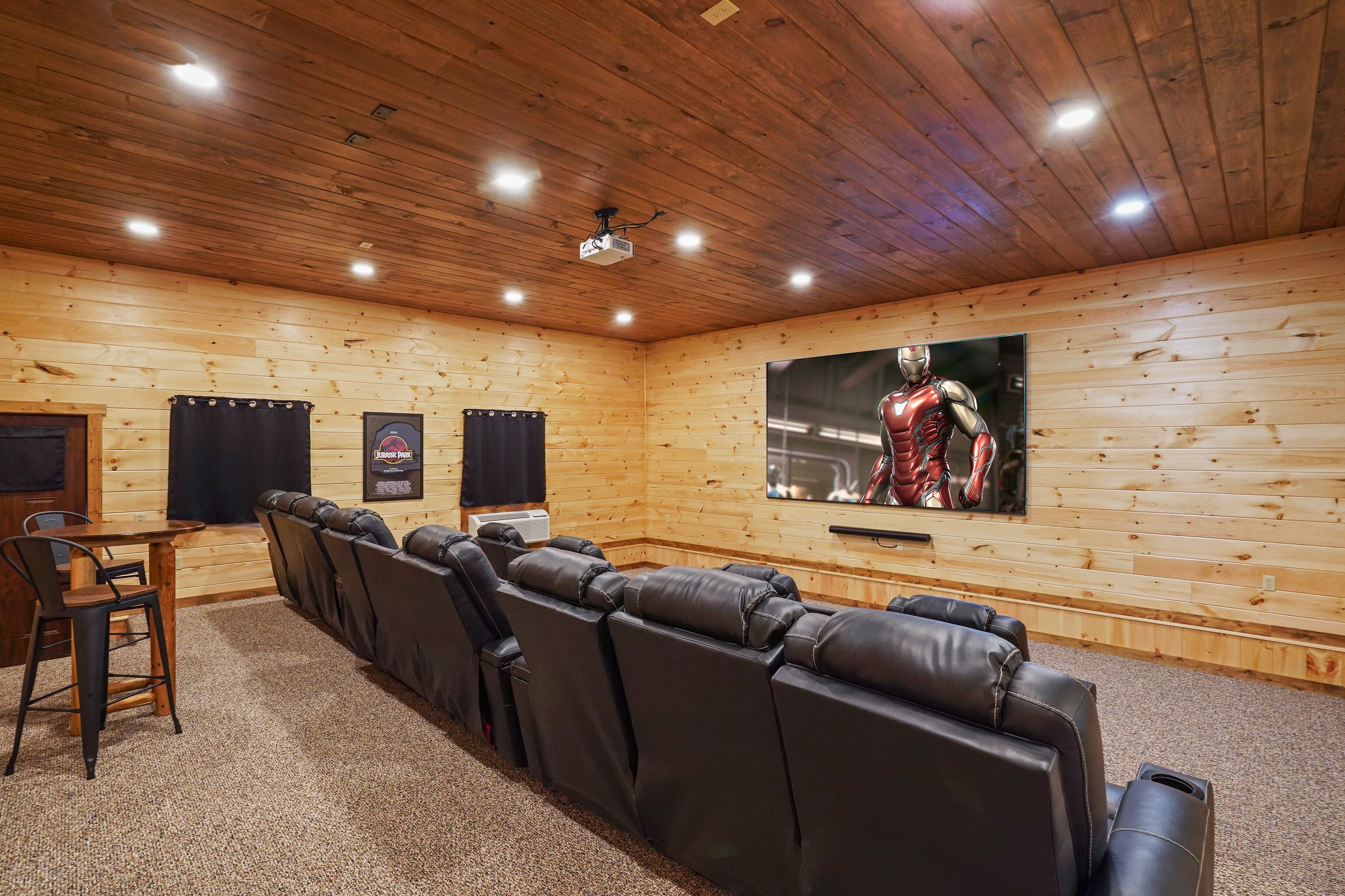 Una habitación con paneles de madera, un televisor de pantalla plana grande, asientos de cuero reclinables, una mesita y dos altavoces.