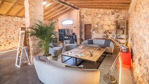 A rustic stone-walled room with a high ceiling, furnished with sofas and a coffee table, and includes a television and bookshelves. - Petit Hotel Son Perdiu Agroturismo (Llucmajor)