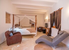 Un dormitorio con cama con dosel, un escritorio con computadora, un televisor y dos sillones.