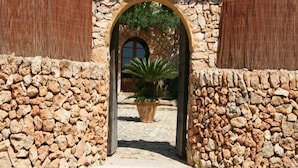 A stone archway leading to a courtyard with a potted plant and a view of a building with a window. - Petit Hotel Son Perdiu Agroturismo (Llucmajor)