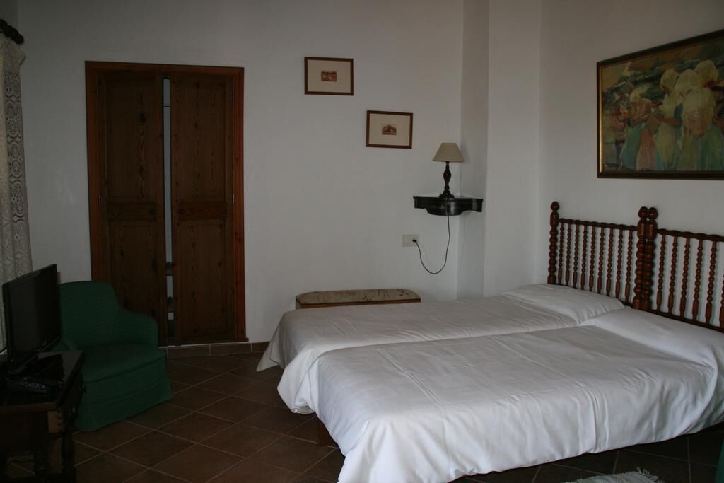 Ein Schlafzimmer mit zwei Betten, einem grünen Sessel, einem Fernseher und einem Bild an der Wand.