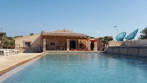 A swimming pool with a stone building in the background, a white fence, and two blue chairs. - Petit Hotel Son Perdiu Agroturismo (Llucmajor)