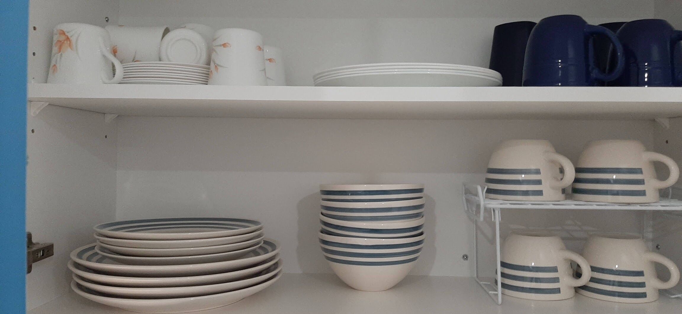 A storage area with shelves holding plates, bowls, and mugs.