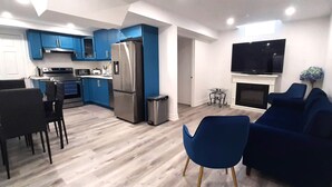 A modern kitchen with blue cabinets, a stainless steel refrigerator, and a dining area with black chairs. - Adorable 2 bedrooms, 2 washrooms, 2 parking spots apartment (Newmarket)