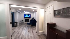 A hallway with a television, a blue chair, and a sign that says "This is Us". - Adorable 2 bedrooms, 2 washrooms, 2 parking spots apartment (Newmarket)