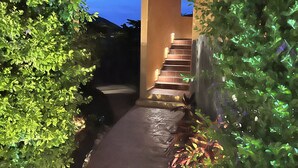 A pathway leading to a building entrance, surrounded by greenery and illuminated steps. - Your Own Private Rooftop Paradise — Hammocks, Ocean Views & Steps from the Beach (Playa Los Cerritos)