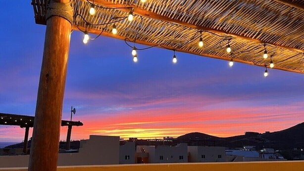 A sunset view from a rooftop with a thatched roof and string lights. - Your Own Private Rooftop Paradise — Hammocks, Ocean Views & Steps from the Beach (Playa Los Cerritos)