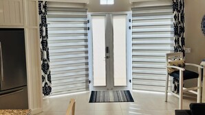 A modern kitchen with a built-in refrigerator, a dining area with a table and chairs, and a large sliding door with patterned curtains. - Your Own Private Rooftop Paradise — Hammocks, Ocean Views & Steps from the Beach (Playa Los Cerritos)